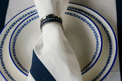 22 Maggio Istanbul Marinaio  Linen Napkin Set of 4-White napkin with a blue stripe and decorative ring on a blue and white patterned plate.