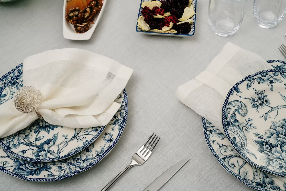 22 Maggio Istanbul Sereno Linen Napkin Set of 4-Set table with blue and white floral plates, silverware, and napkins on a gray surface.