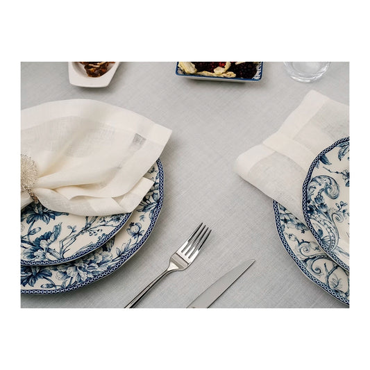 22 Maggio Istanbul Sereno Linen Tablecloth-Dining table setting with blue and white patterned plates, silverware, and white napkins on a gray tablecloth.