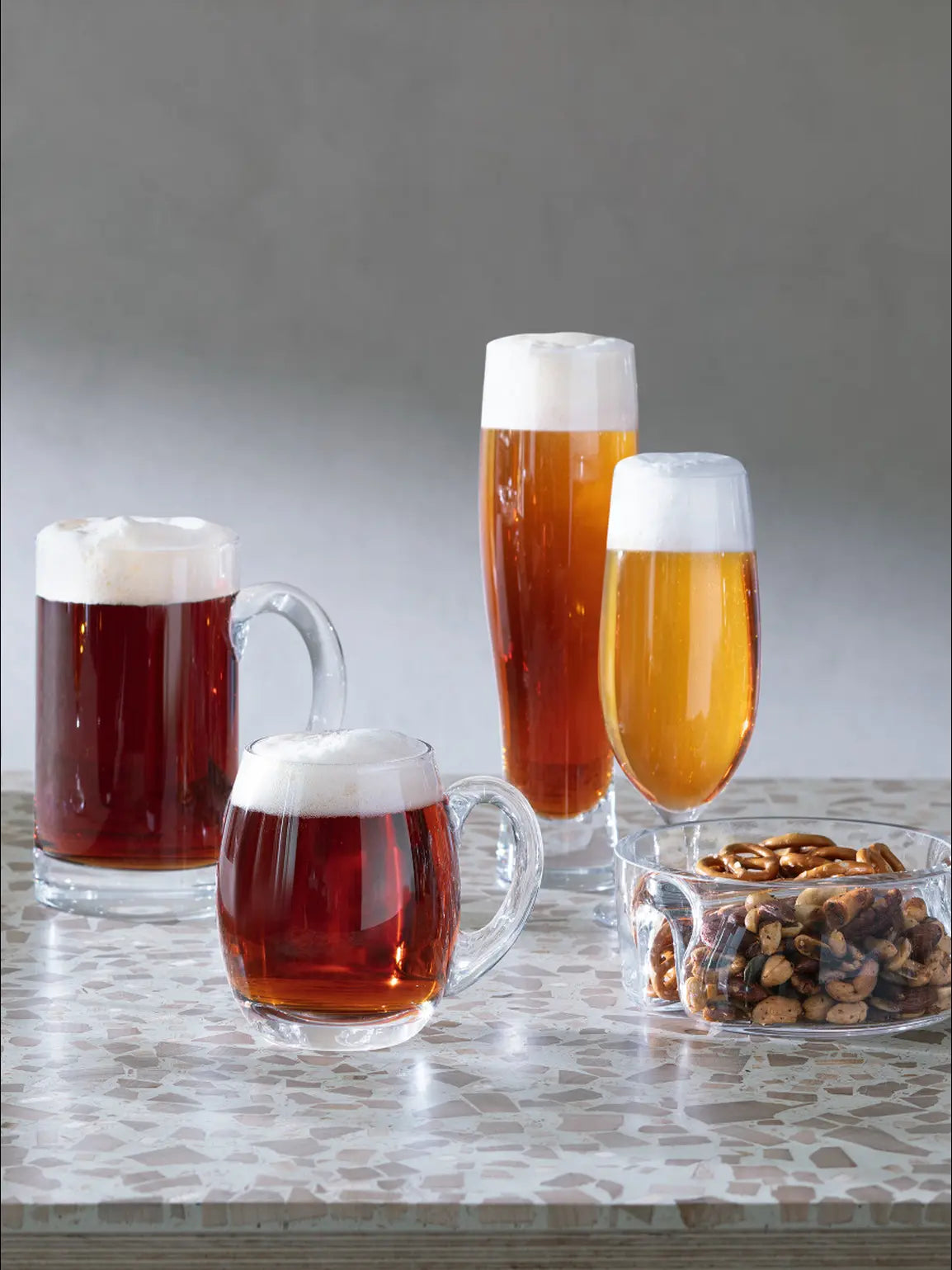 Bar Pilsner Glass for serving beer with perfect pour-Three glasses of beer with foam and a bowl of nuts on a speckled surface.