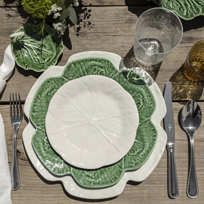 Bordallo Pinheiro Cabbage Dinner Plate-Green and white ceramic plate on a wooden table with cutlery and glasses.