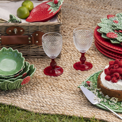 Bordallo Strawberries Bowl – Artisan Fruit Ceramic UAE-Outdoor picnic setup with red and green dishes, glasses, and a cake on a woven mat.