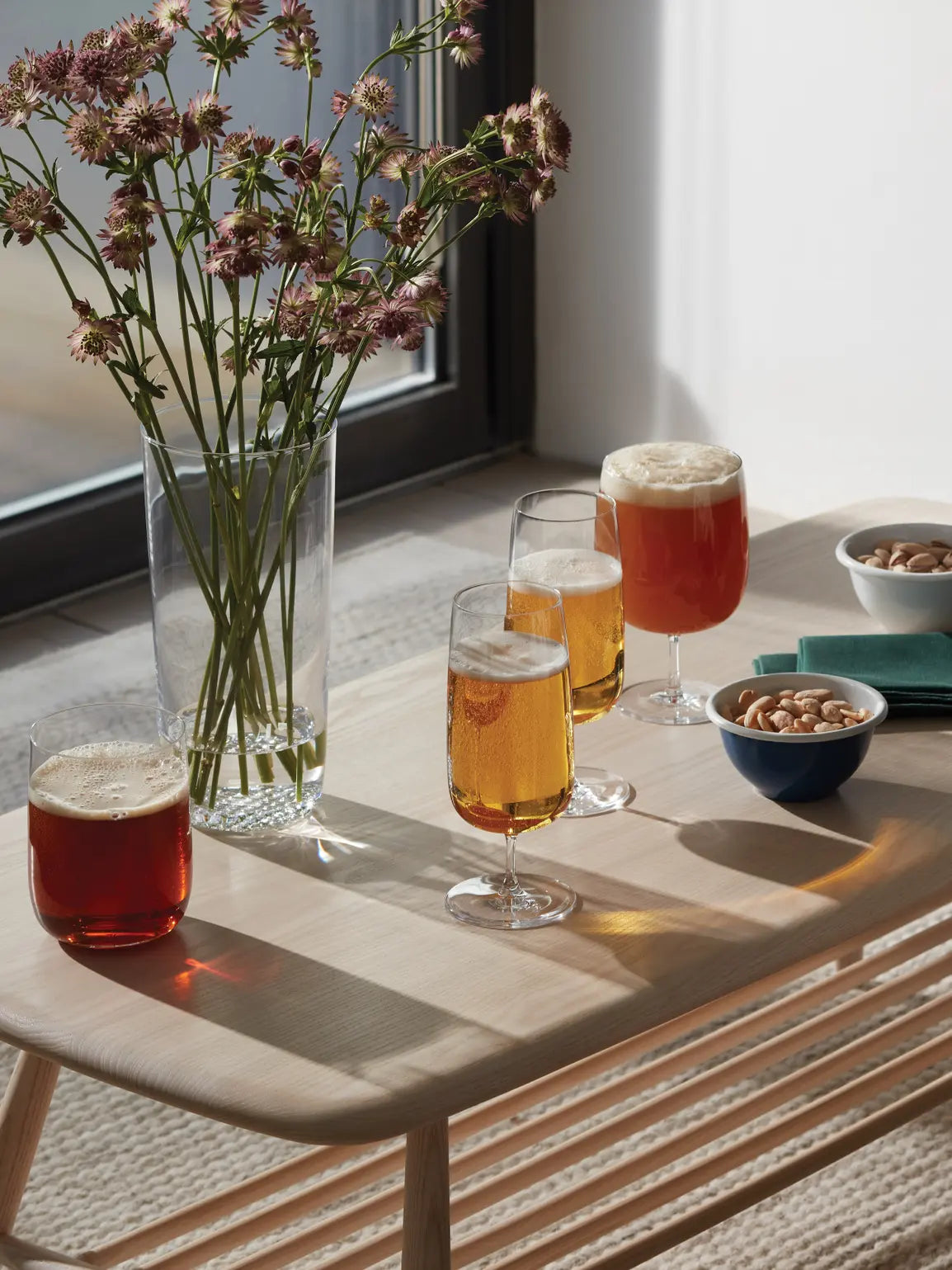 Borough Pilsner Glass for elegant beer serving-Table with glasses of beer, a vase of flowers, and bowls of snacks.