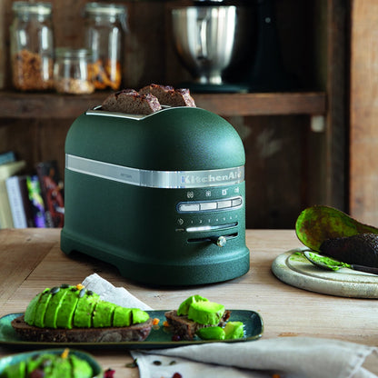 Green KitchenAid Bread toasteron a wooden table with avocado toast and ingredients.