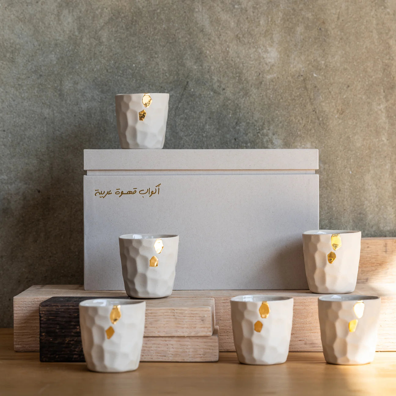 Set of white ceramic Cawa Cups with gold accents on a wooden stand against a gray wall.