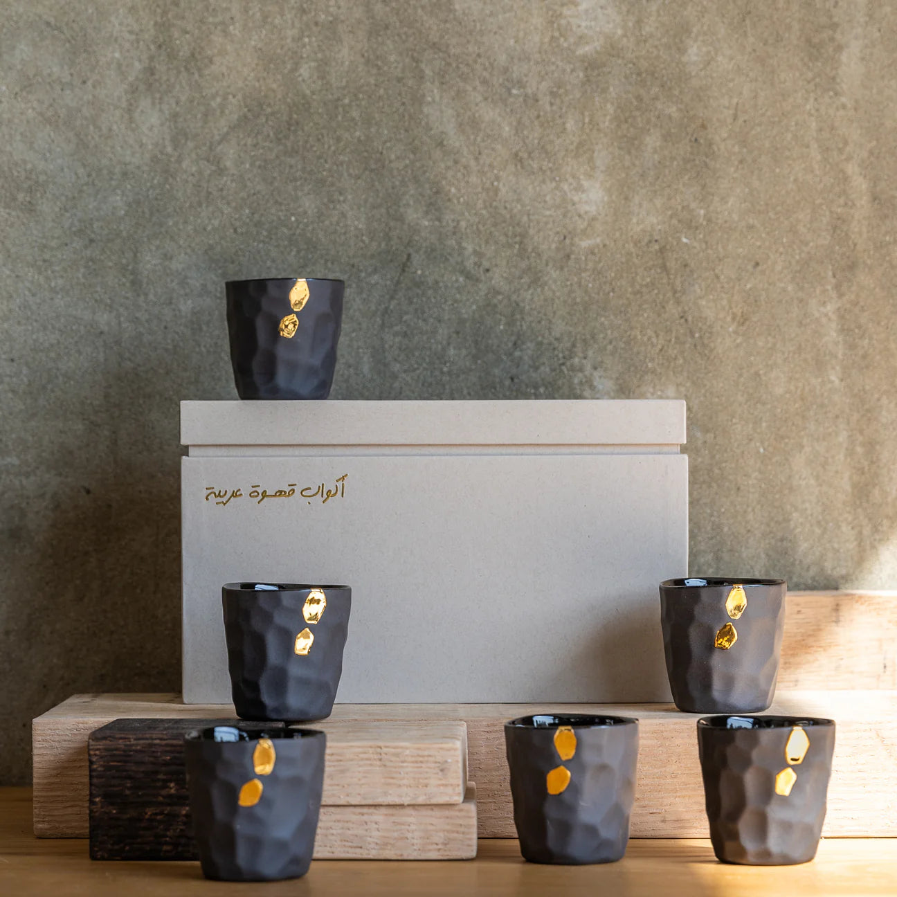 Set of black ceramic Cawa Cups with gold accents on a wooden stand against a textured wall.