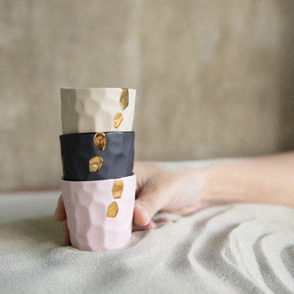 Person holding a cylindrical ceramic Cawa Cups with gold accents on a textured surface
