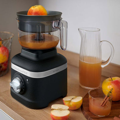 Black KitchenAid juicer with apples and juice on a wooden surface