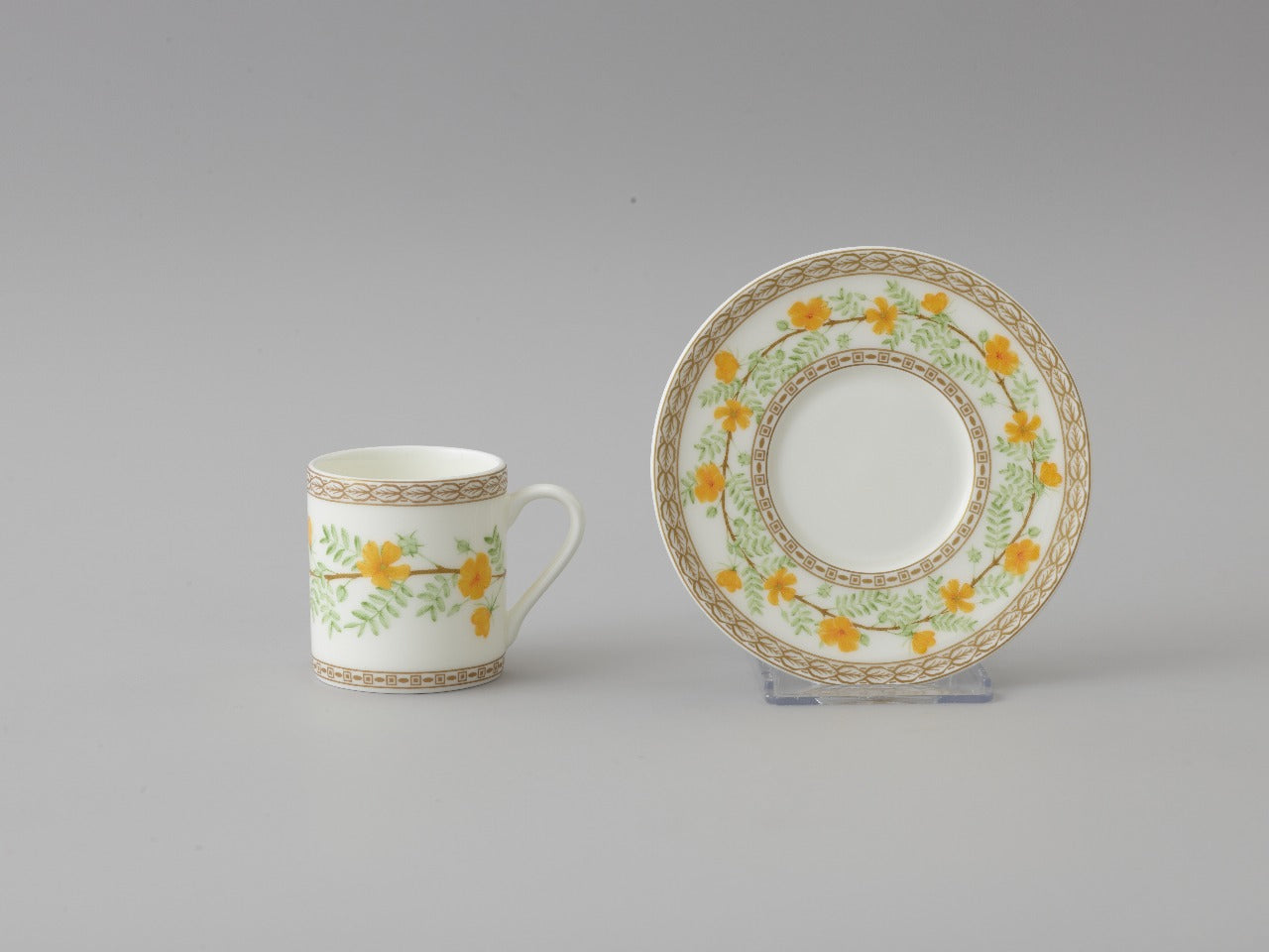 Collation formation curation A white ceramic cup with green and yellow floral patterns, accompanied by a matching saucer.