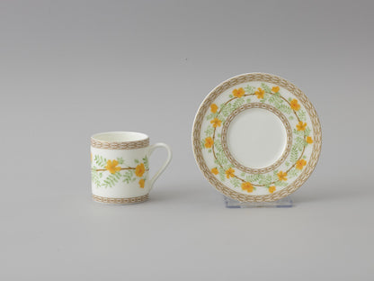 Collation formation curation A white ceramic cup with green and yellow floral patterns, accompanied by a matching saucer.