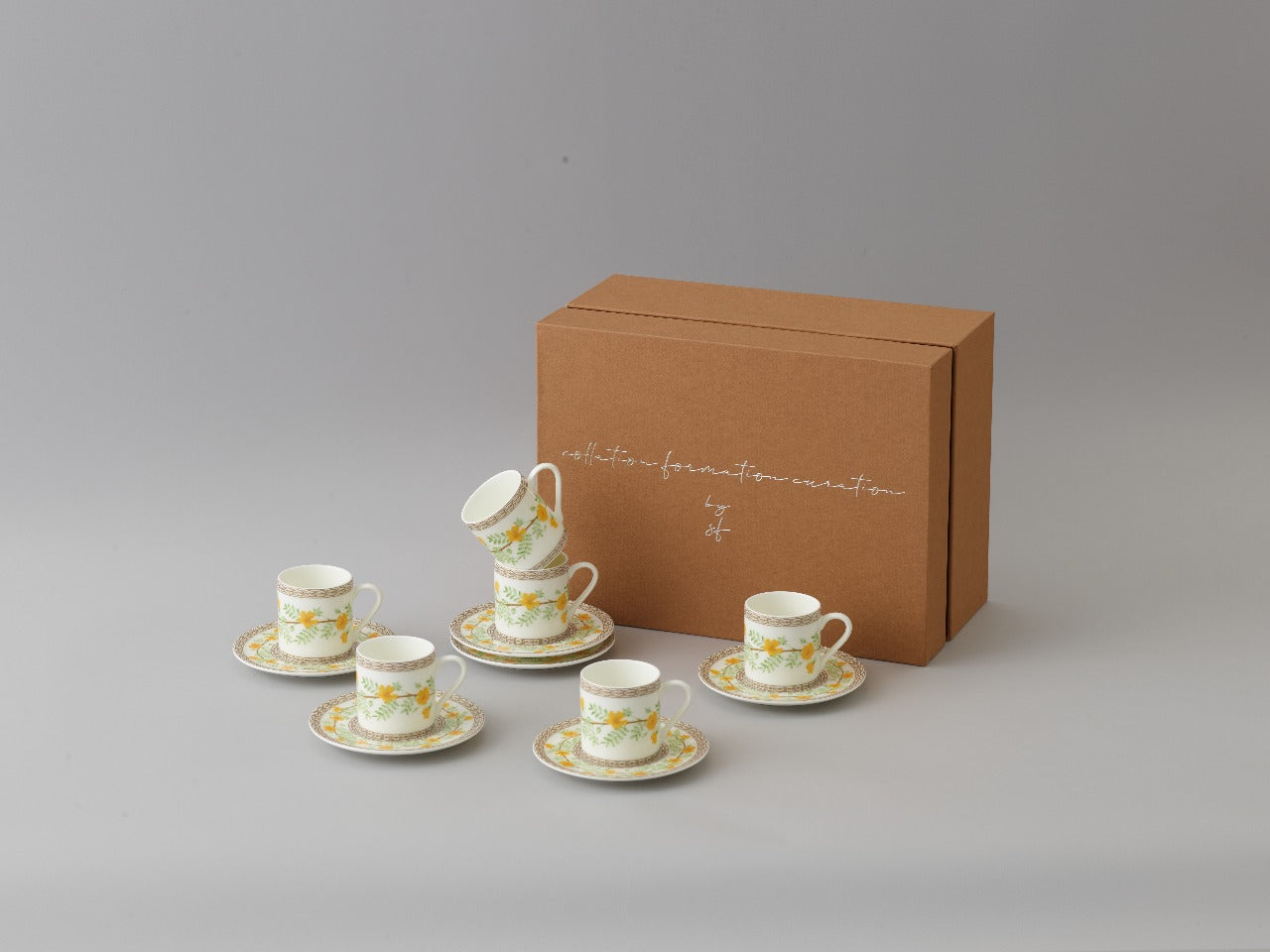 Collation formation curation A white ceramic cup with green and yellow floral patterns, accompanied by a matching saucer with box