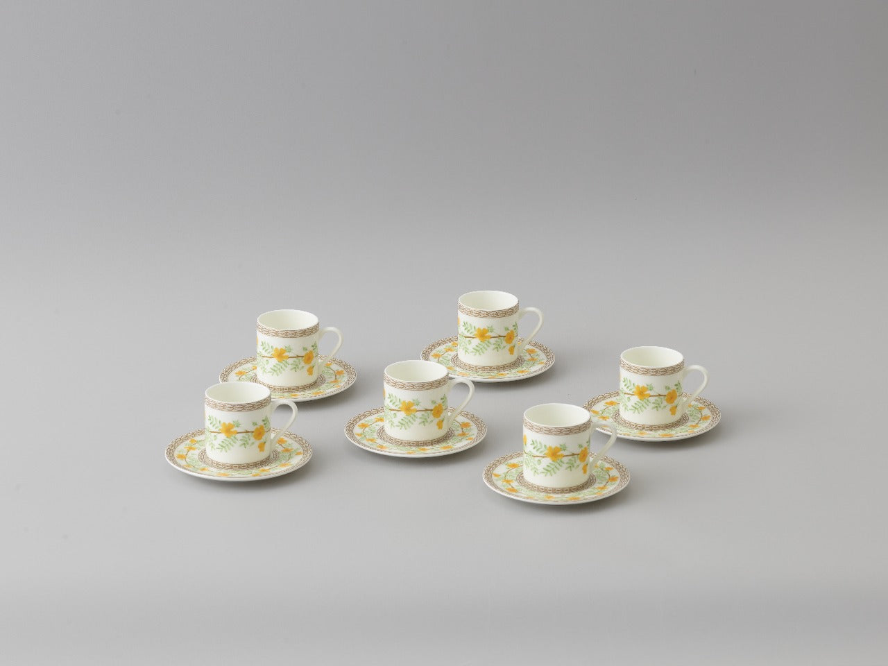 Collation formation curation A white ceramic cup with green and yellow floral patterns, accompanied by a matching saucer.