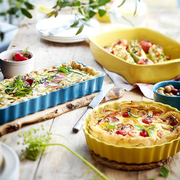 Emile Henry Deep Round Tart Dish, 24cm-Dishes of food on a wooden table with a yellow tart and blue dish in the background.
