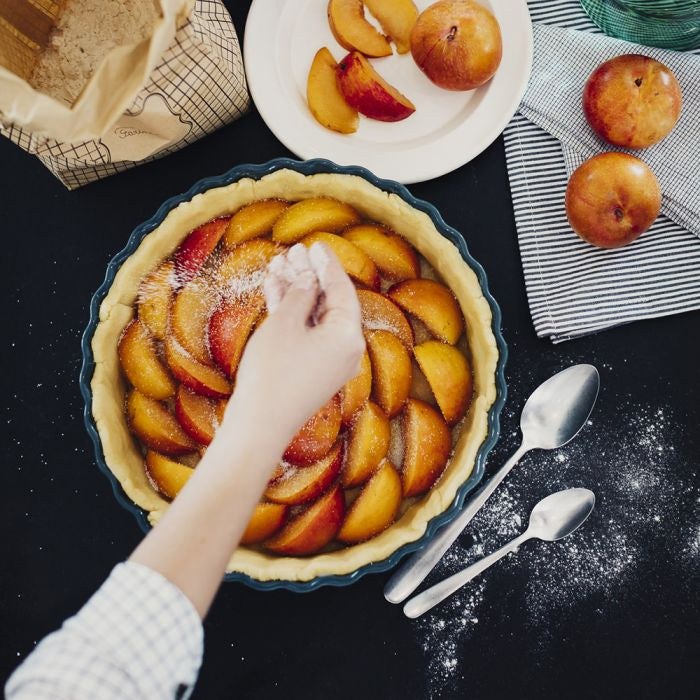 Emile Henry Deep Round Tart Dish, 24cm-Person preparing a peach pie with peaches on a table