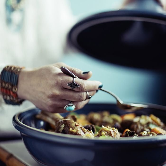 Emile Henry Flame Tagine-Person holding a spoon over a dish of food with a blurred background