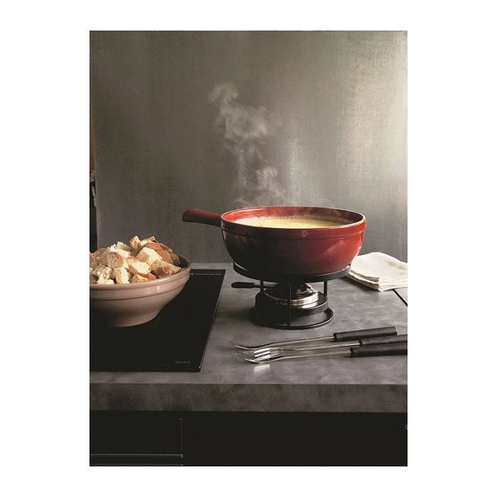 Emile Henry Fondue Set-Red fondue pot with steam, bowl of bread, and utensils on a gray surface.