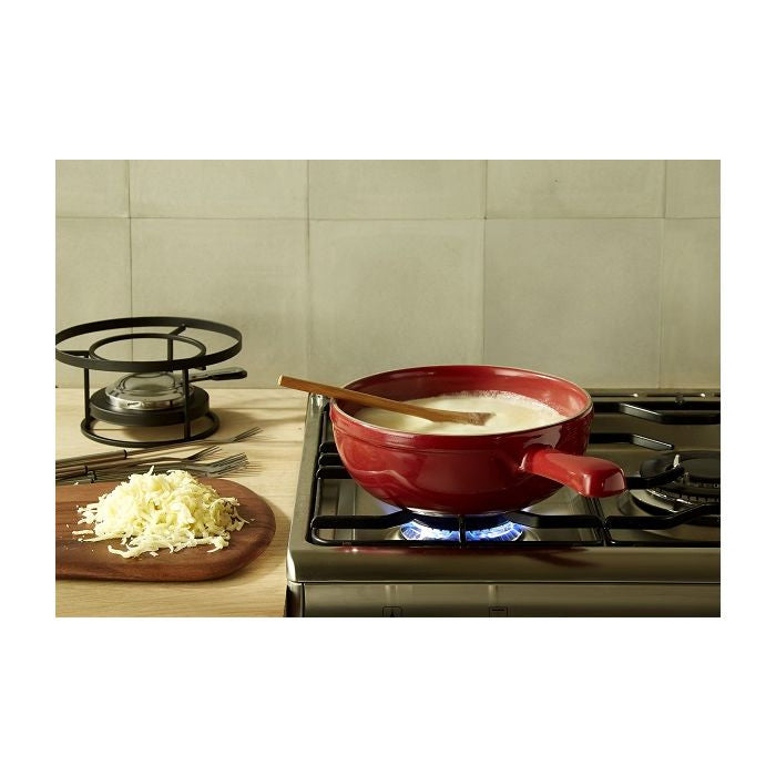Emile Henry Fondue Set-Red pot on a stove with cheese and a wooden spoon, set against a tiled wall.