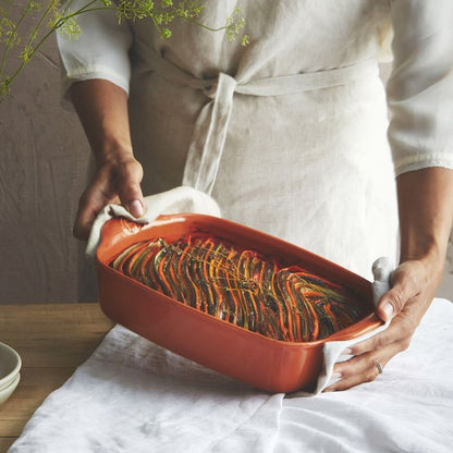 Emile Henry Rectangular Oven Dish-Person holding a red ceramic baking dish with a vegetable dish on a wooden surface.