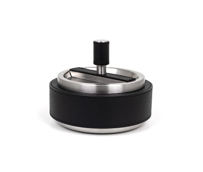 A round, stainless steel ashtray with a black leather cover and a central spinning element.