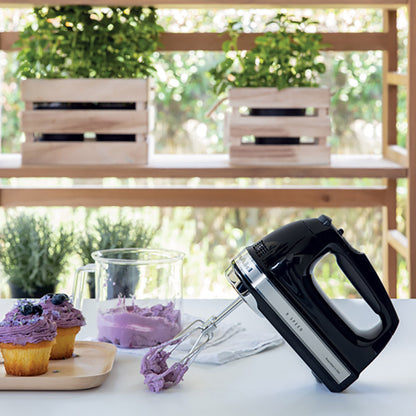 Black hand mixer with purple frosting on a table outdoors