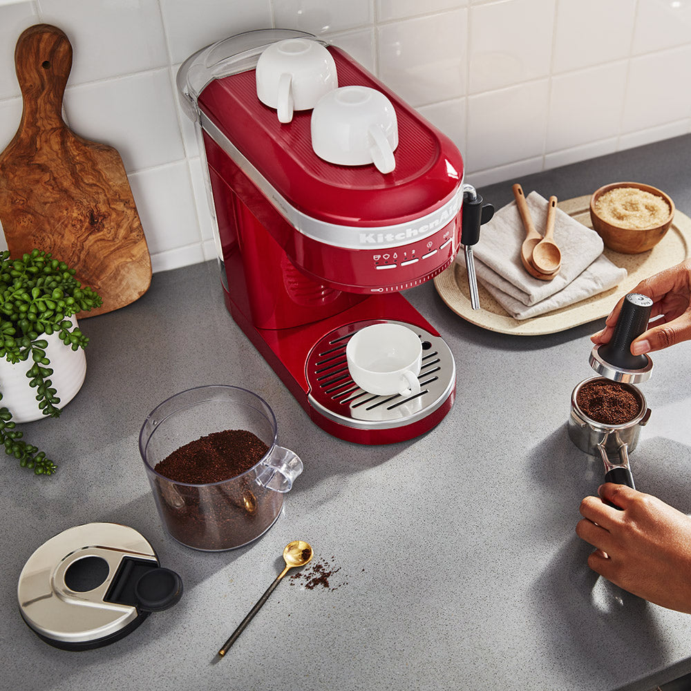 Red coffee machine on a kitchen counter with coffee beans and a person preparing coffee.