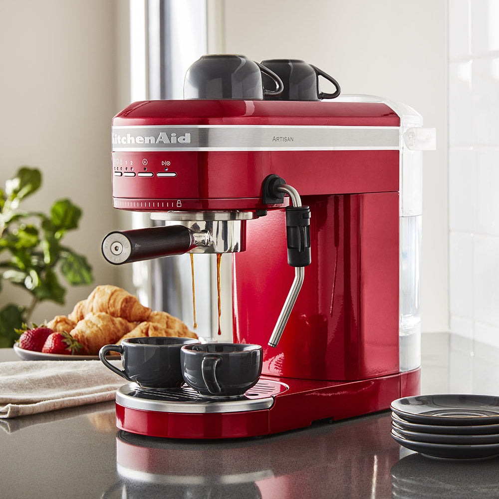 Red KitchenAid espresso machine on a kitchen counter with coffee being dispensed.