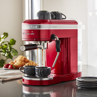 Red KitchenAid espresso machine on a kitchen counter with coffee being dispensed.