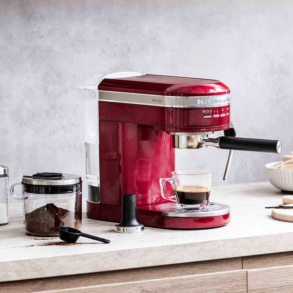Red espresso machine on a kitchen counter with a glass of coffee.