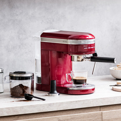 Red espresso machine on a kitchen counter with a glass of coffee.
