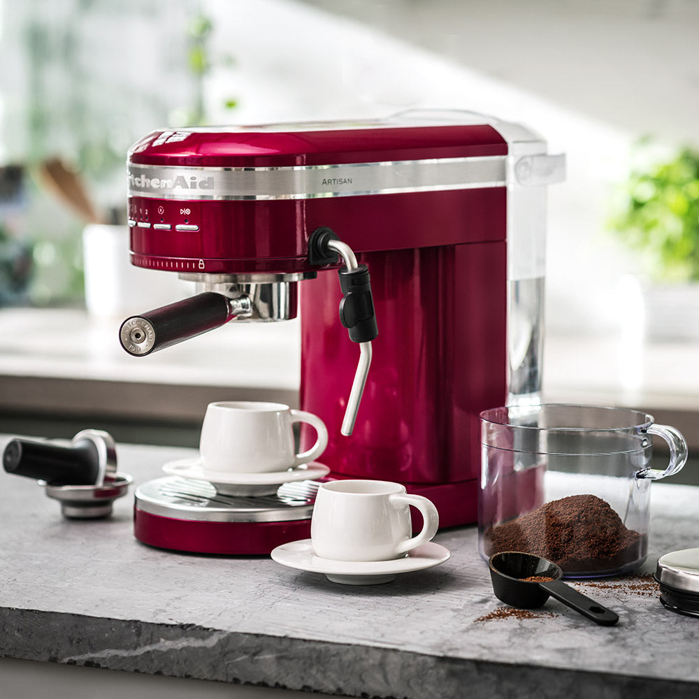 Red KitchenAid espresso machine on a kitchen counter with coffee cups and ingredients.