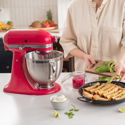 Red stand mixer on a kitchen counter with a person preparing food.