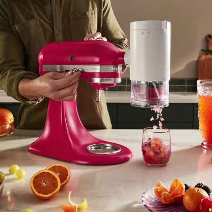 Person using a pink stand mixer to make a fruit smoothie in a kitchen.