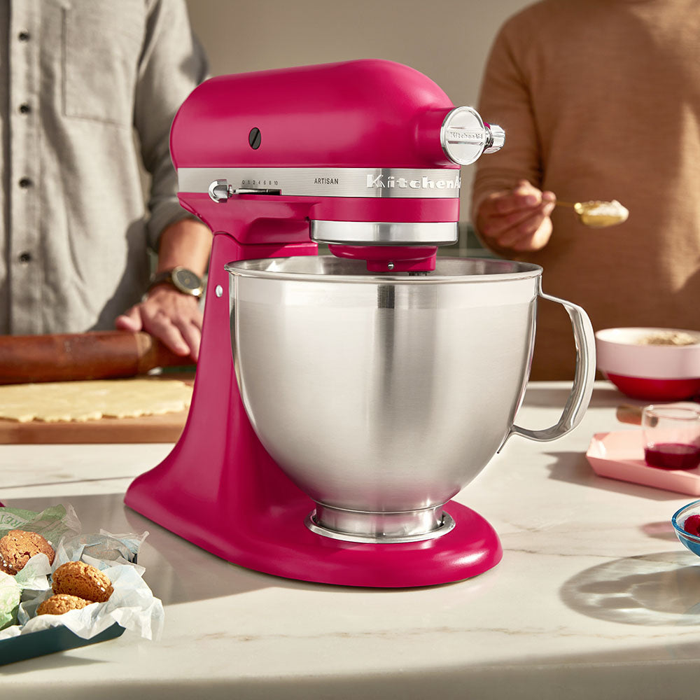 Pink KitchenAid stand mixer on a kitchen counter with people in the background.