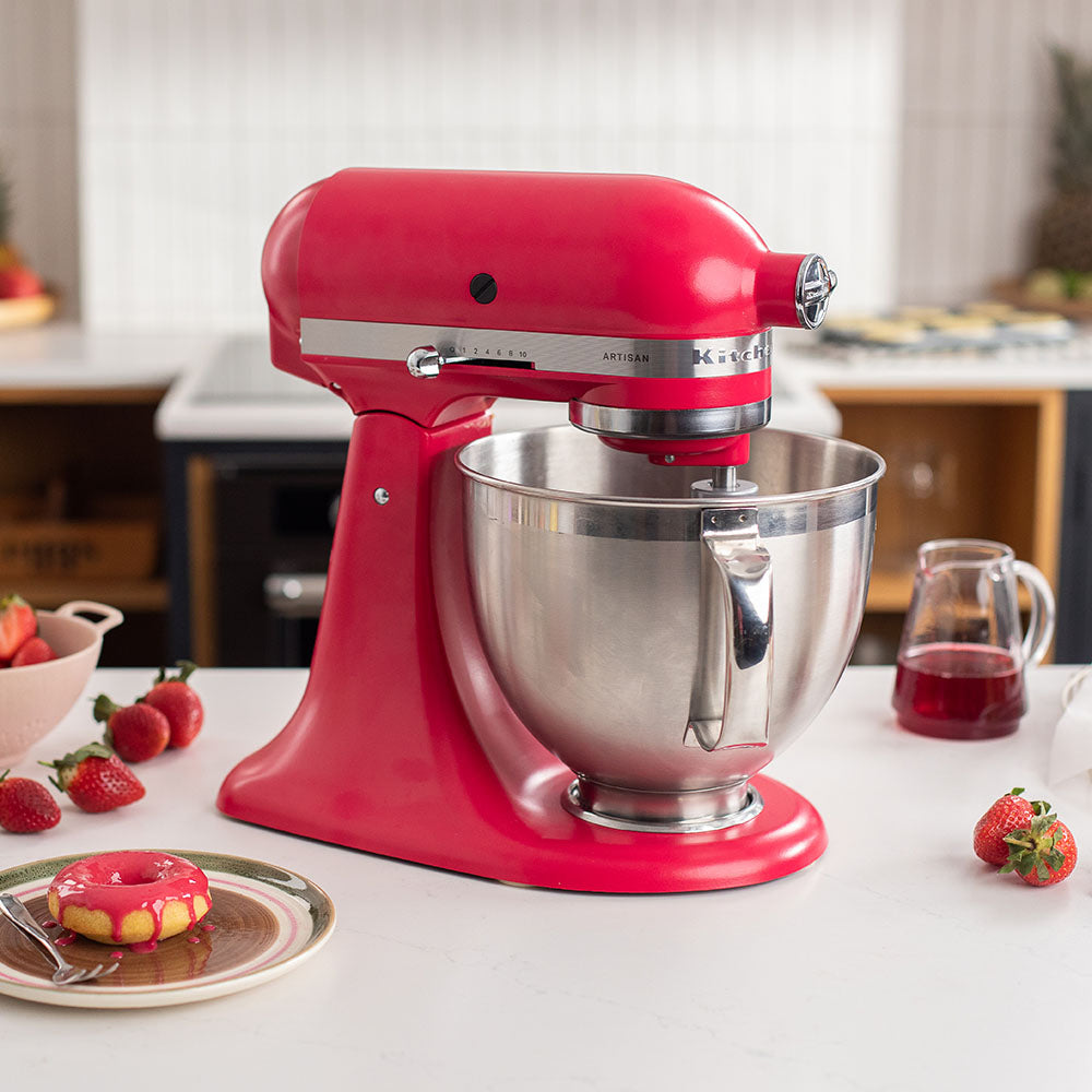 Red stand mixer on a kitchen counter with strawberries and a donut.