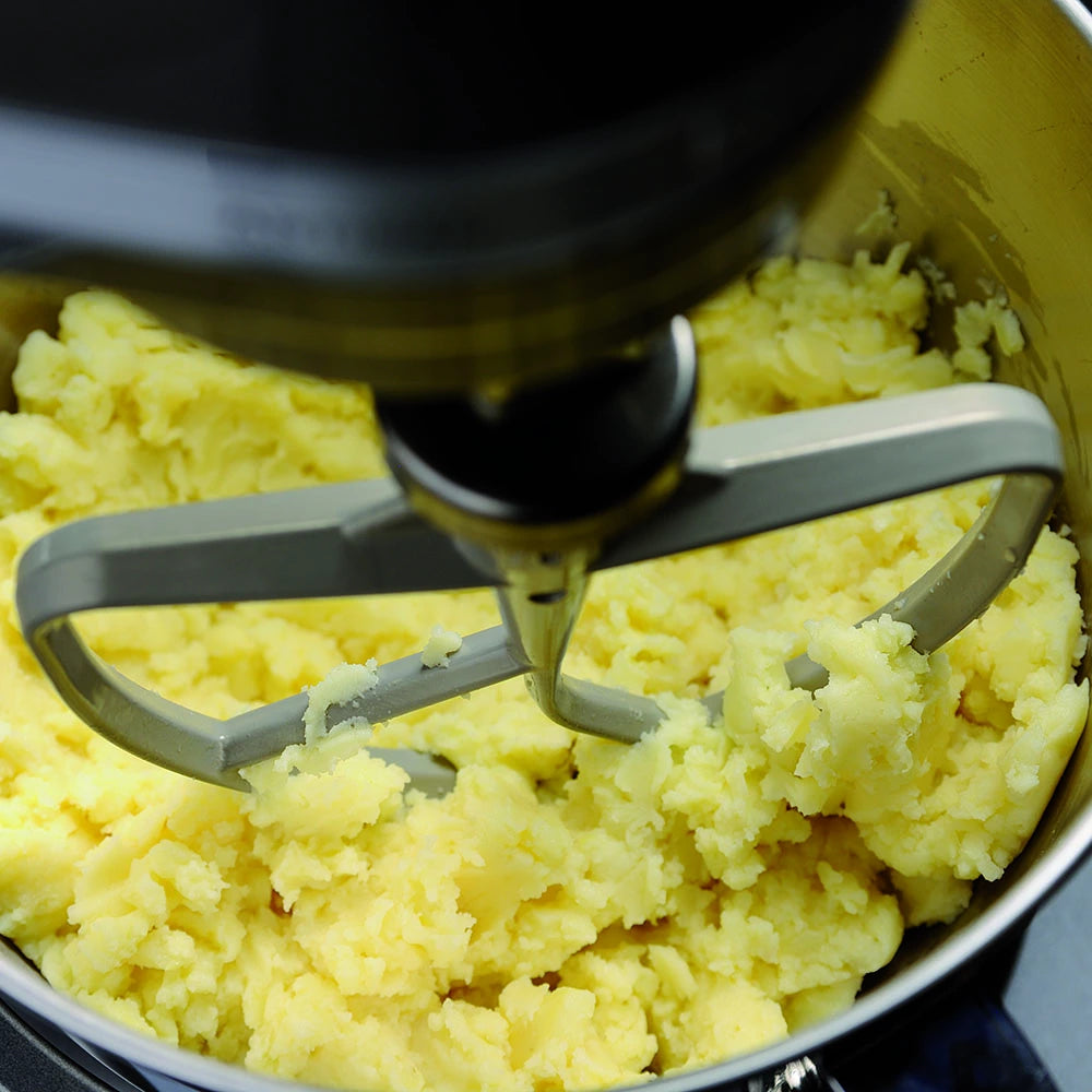 Mashed potatoes being mixed with a kitchen mixer attachment.