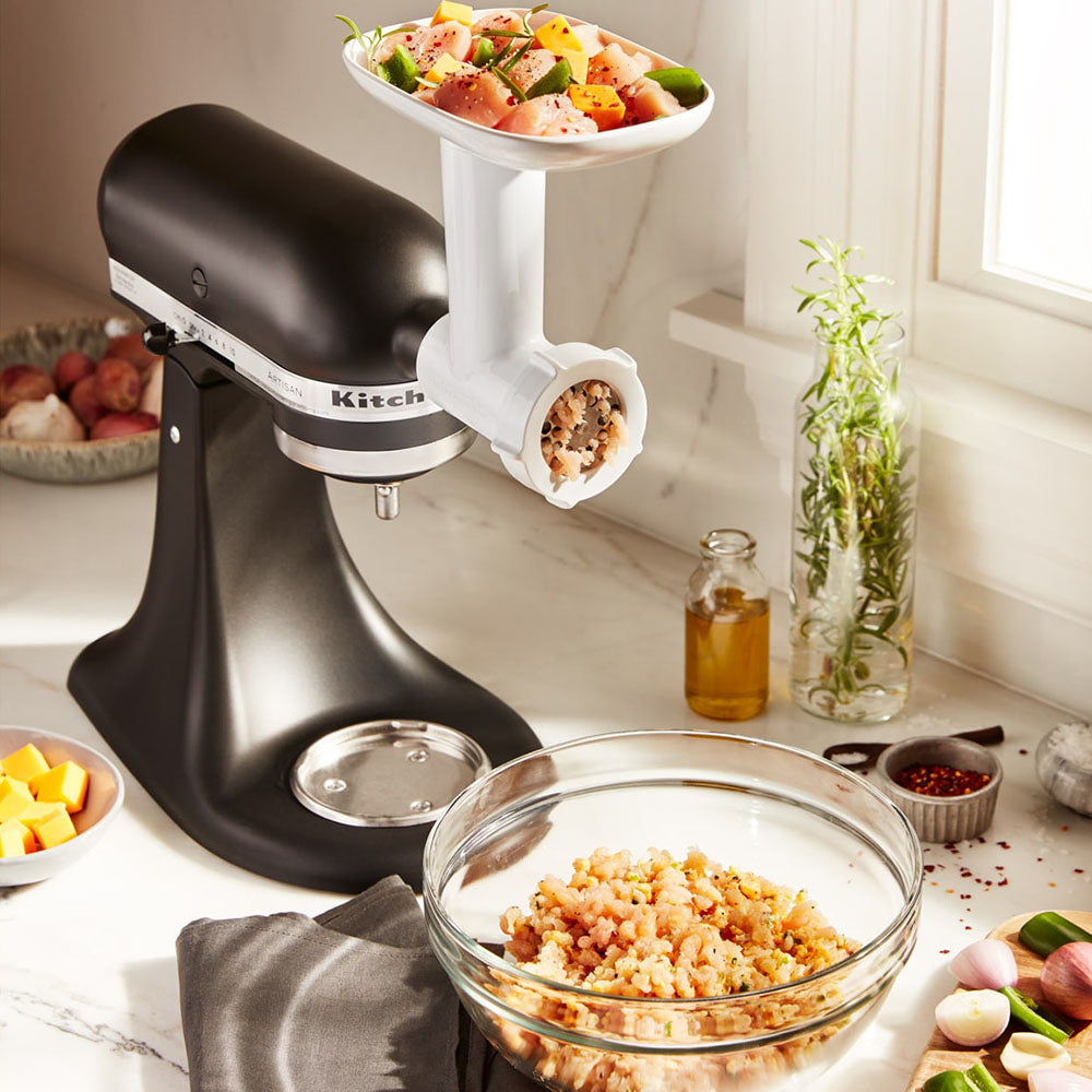 Kitchen stand mixer with meat KitchenAid Food Grinder-attachment on a kitchen counter.