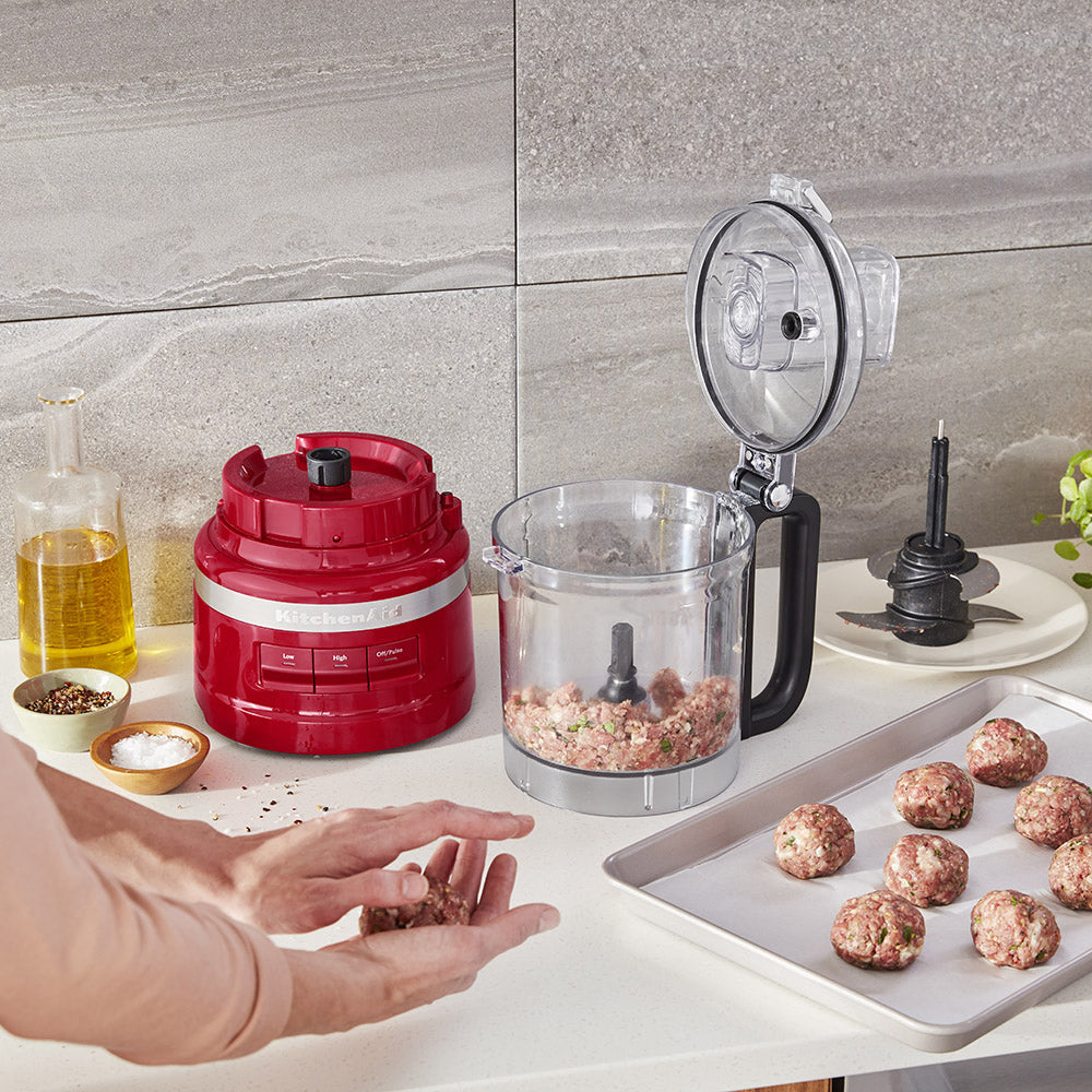 Person making meatballs with a food processor on a kitchen counter.