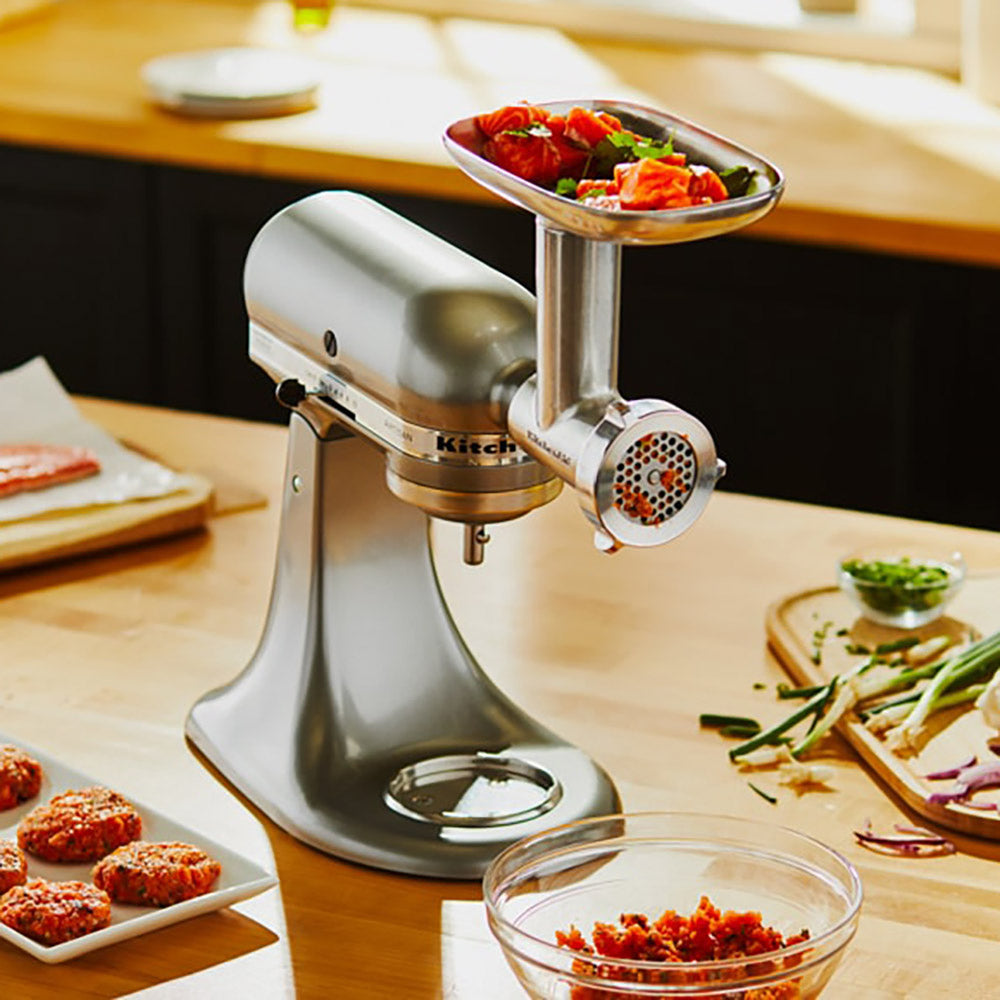 Kitchen stand mixer with meat grinder attachment on a wooden table