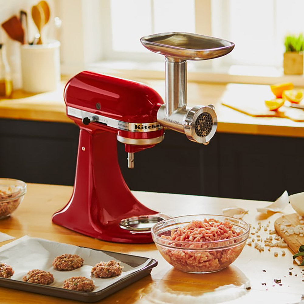 Red KitchenAid stand mixer with meat grinder attachment on a kitchen counter.