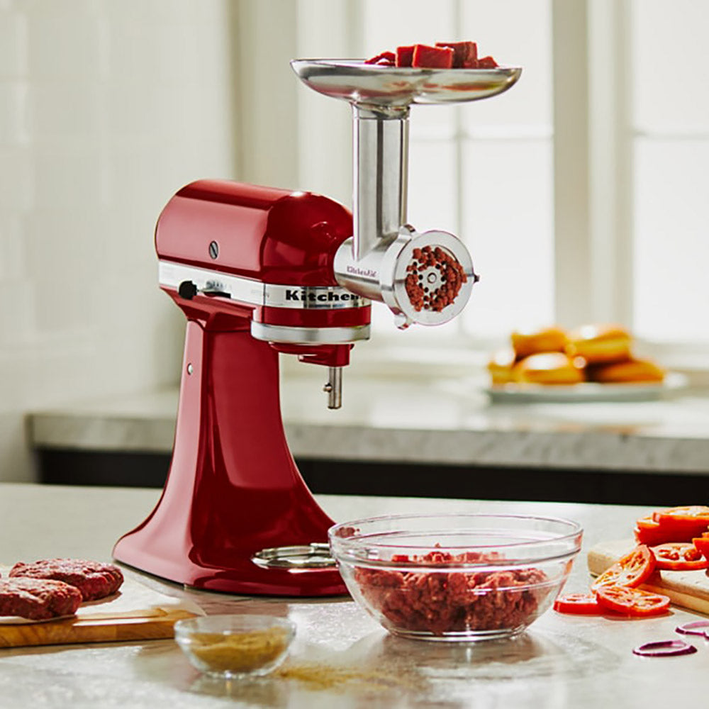Red KitchenAid stand mixer with meat grinder attachment on a kitchen counter.
