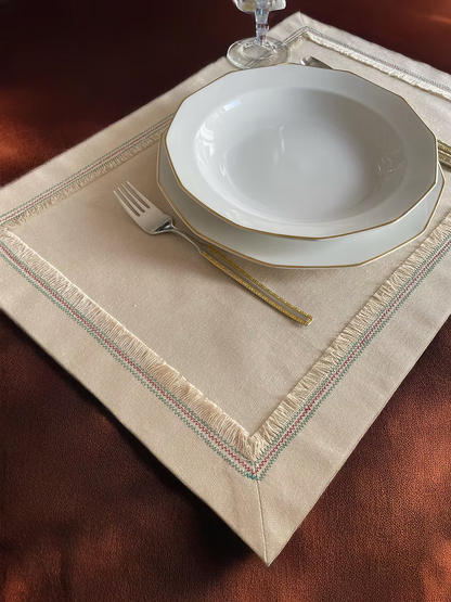 Nappina Placemat Set of 4-White ceramic plates with gold rims on a beige placemat with decorative edge, on a wooden table.