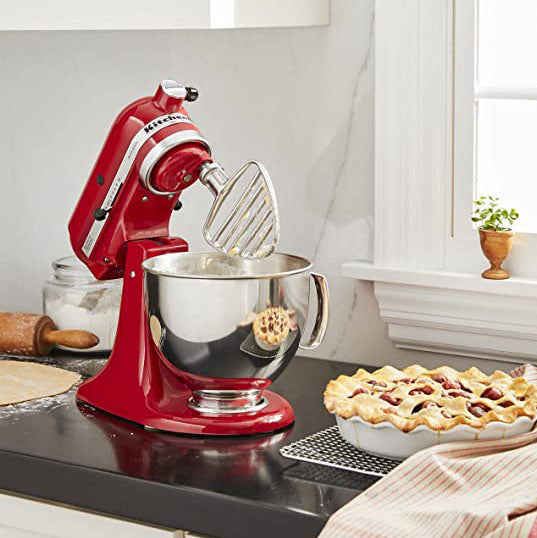Red KitchenAid stand mixer on a kitchen counter with a pie in the background