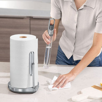 Simplehuman Kitchen Roll Holder with Spray Pump Person cleaning a countertop with a paper towel holder and paper towels in the foreground.