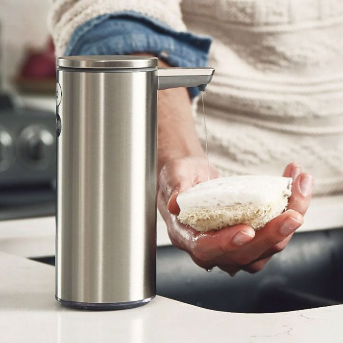 Simplehuman Liquid Dish Soap Person holding a bar of soap next to a stainless steel soap dispenser on a kitchen counter.