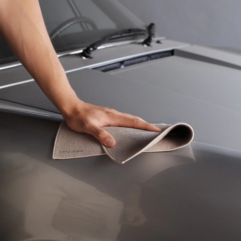 Person cleaning a car's hood with a microfiber cloth.