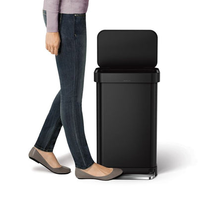 Simplehuman Rectangular Pedal Bin with Liner Pocket Black trash bin with a person standing next to it 