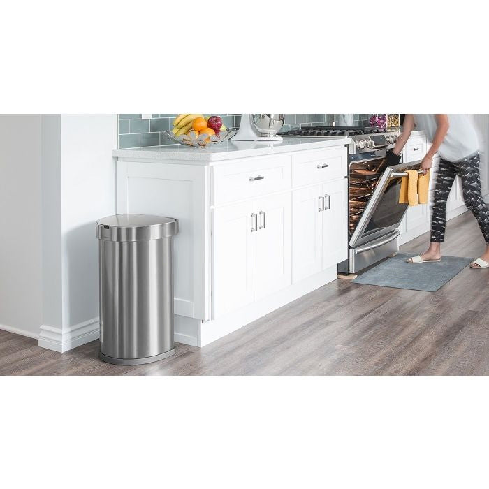 Simplehuman Semi Round Sensor Bin With Liner Pocket-Stainless steel trash can in a kitchen setting with a person opening an oven.