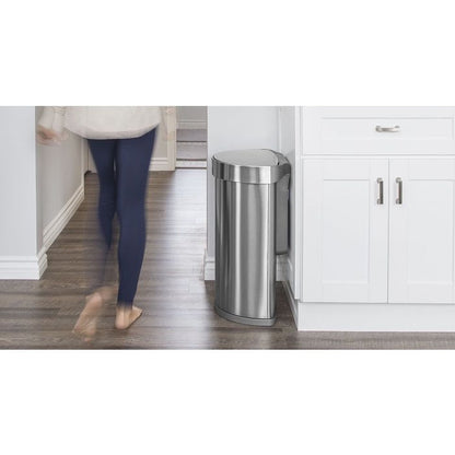 Simplehuman Semi Round Sensor Bin With Liner Pocket-Person walking past a stainless steel trash can in a kitchen.
