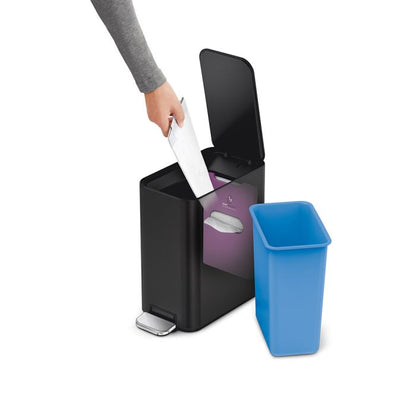 Person disposing of paper into a black trash can with a blue liner.