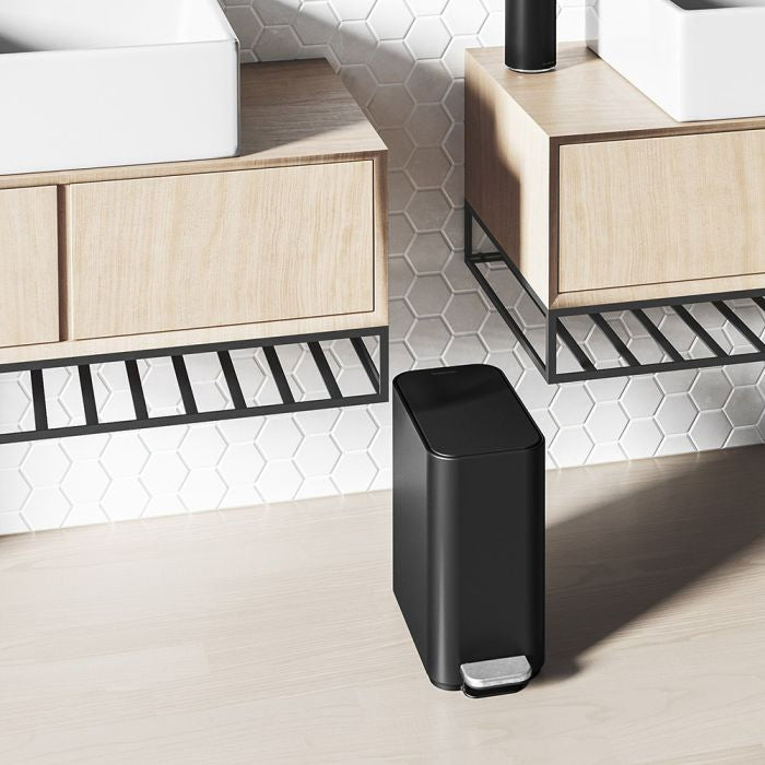 Black trash bin on a light wood floor with a modern interior design background.